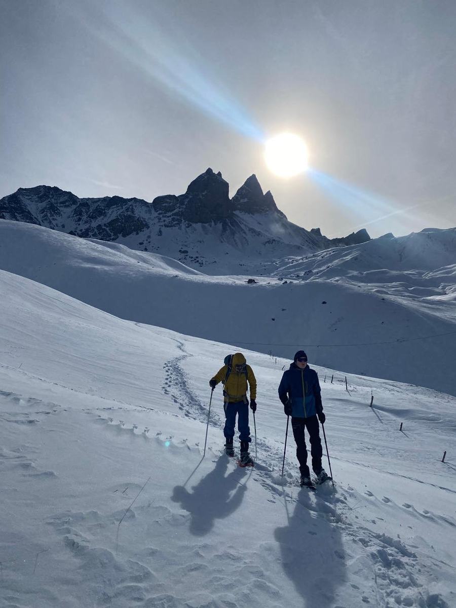 Twee wandelaars op sneeuwschoenen in een besneeuwd berglandschap met tegenlicht